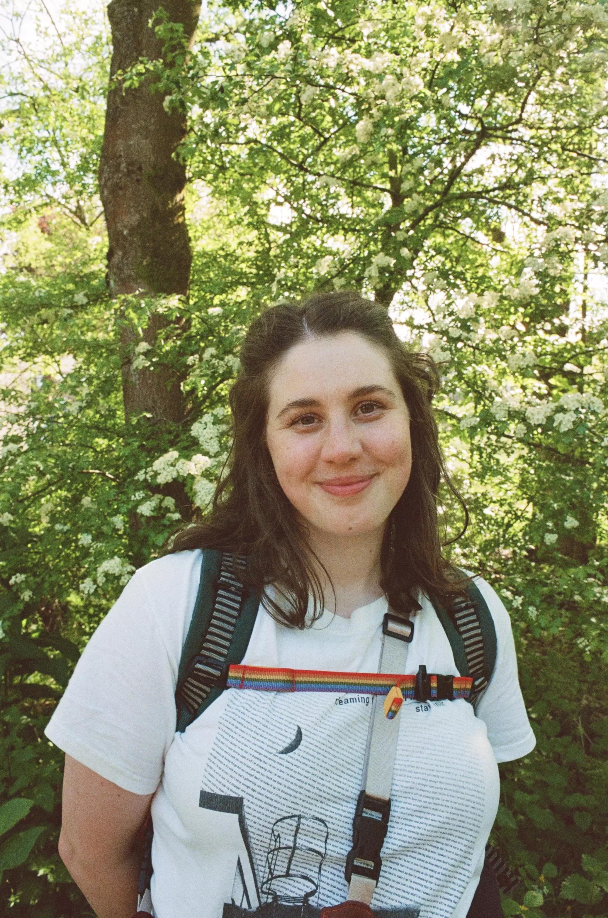 Young female with brunette hair stood infront of a tree and white flowers