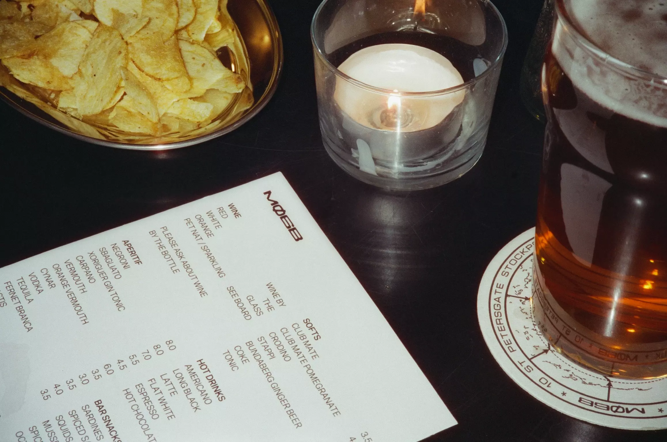 Flash photo of a table with a menu, drink, crisps and a candle alight