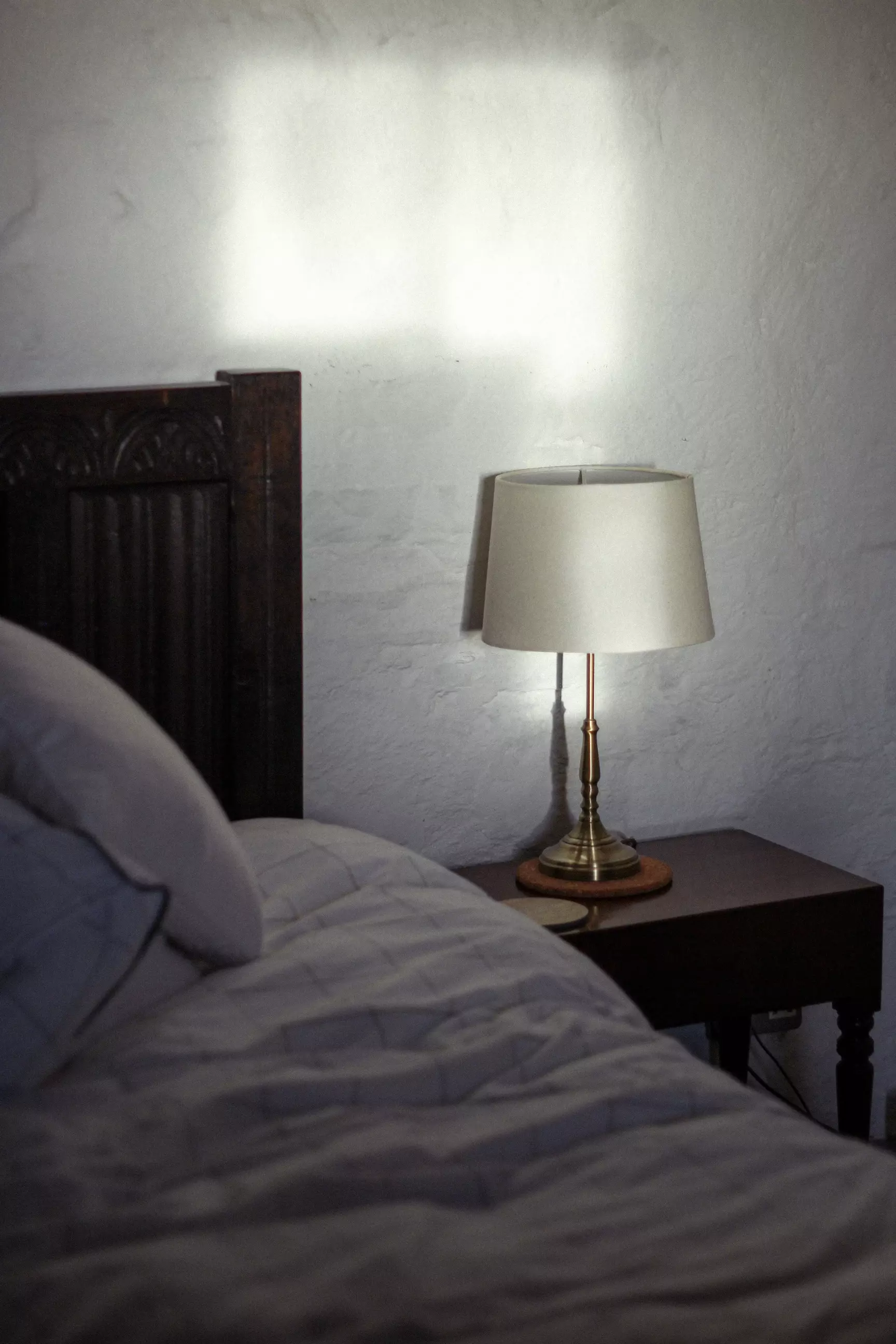 Morning sunshine reflecting onto wall in bedroom with a lamp on side table