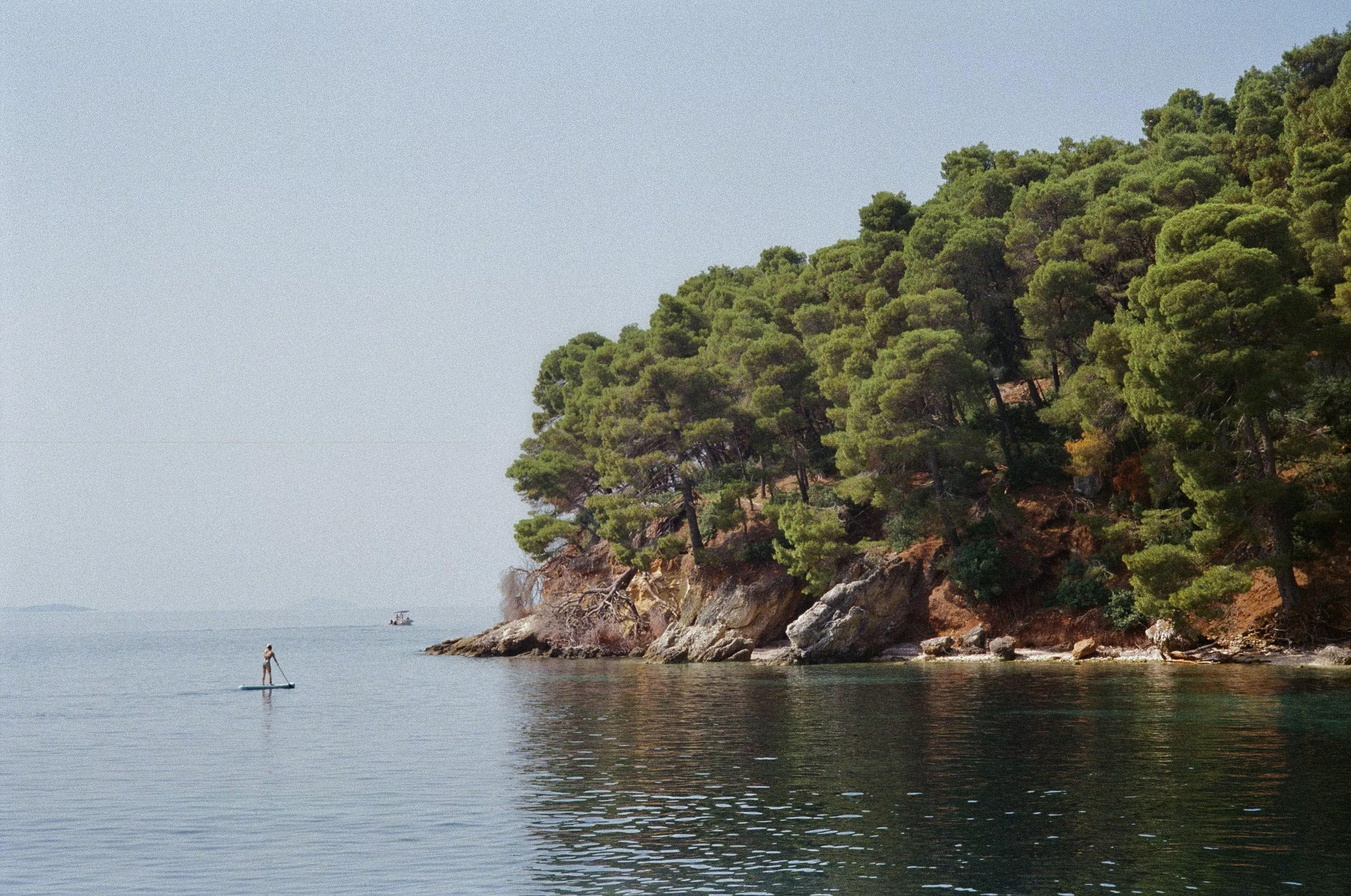 Wide shot of Kalamos Island from the sea and a paddleboarder in the distance