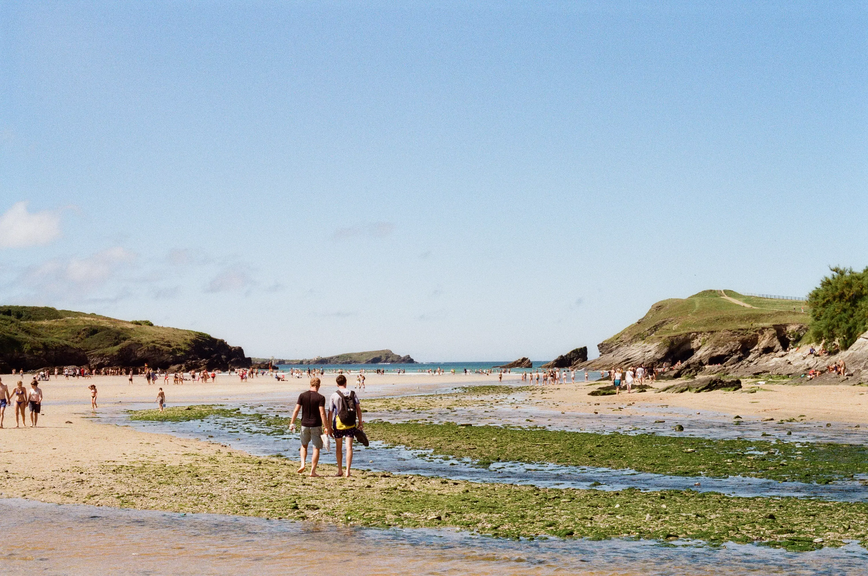 Lots of people walking across a beach in Newquay on a sunny day with the sea in the distance