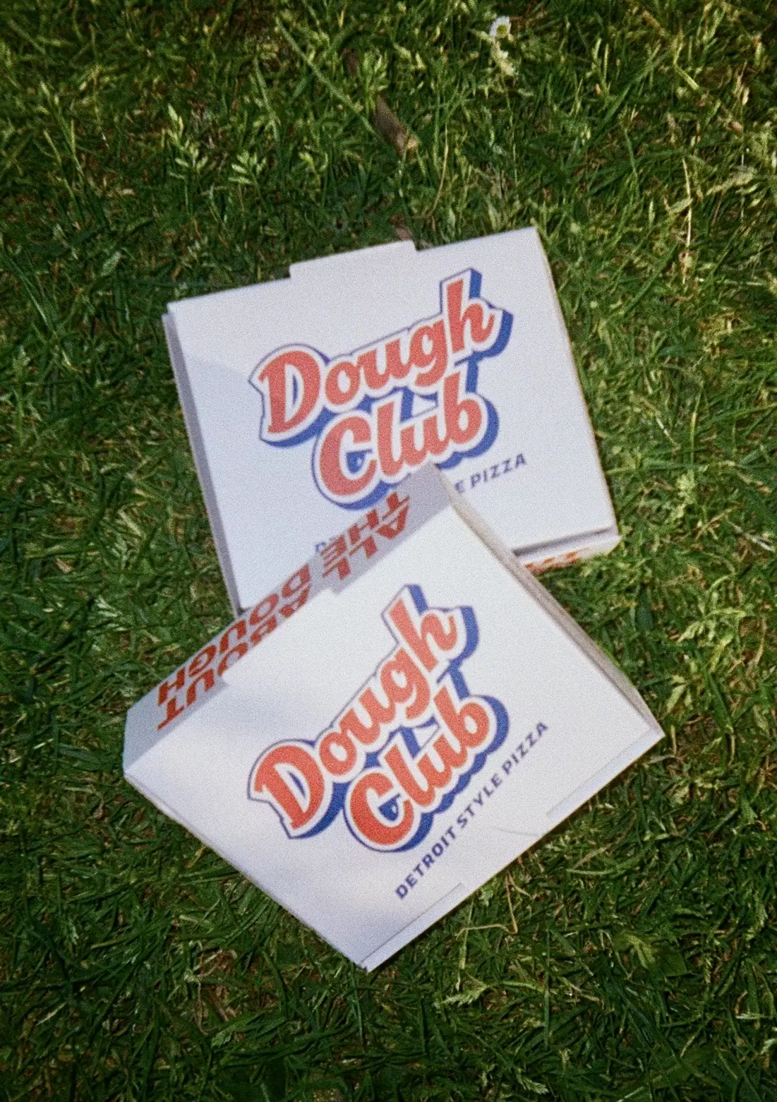 Dough Club Pizza packaging set against a white tiled wall