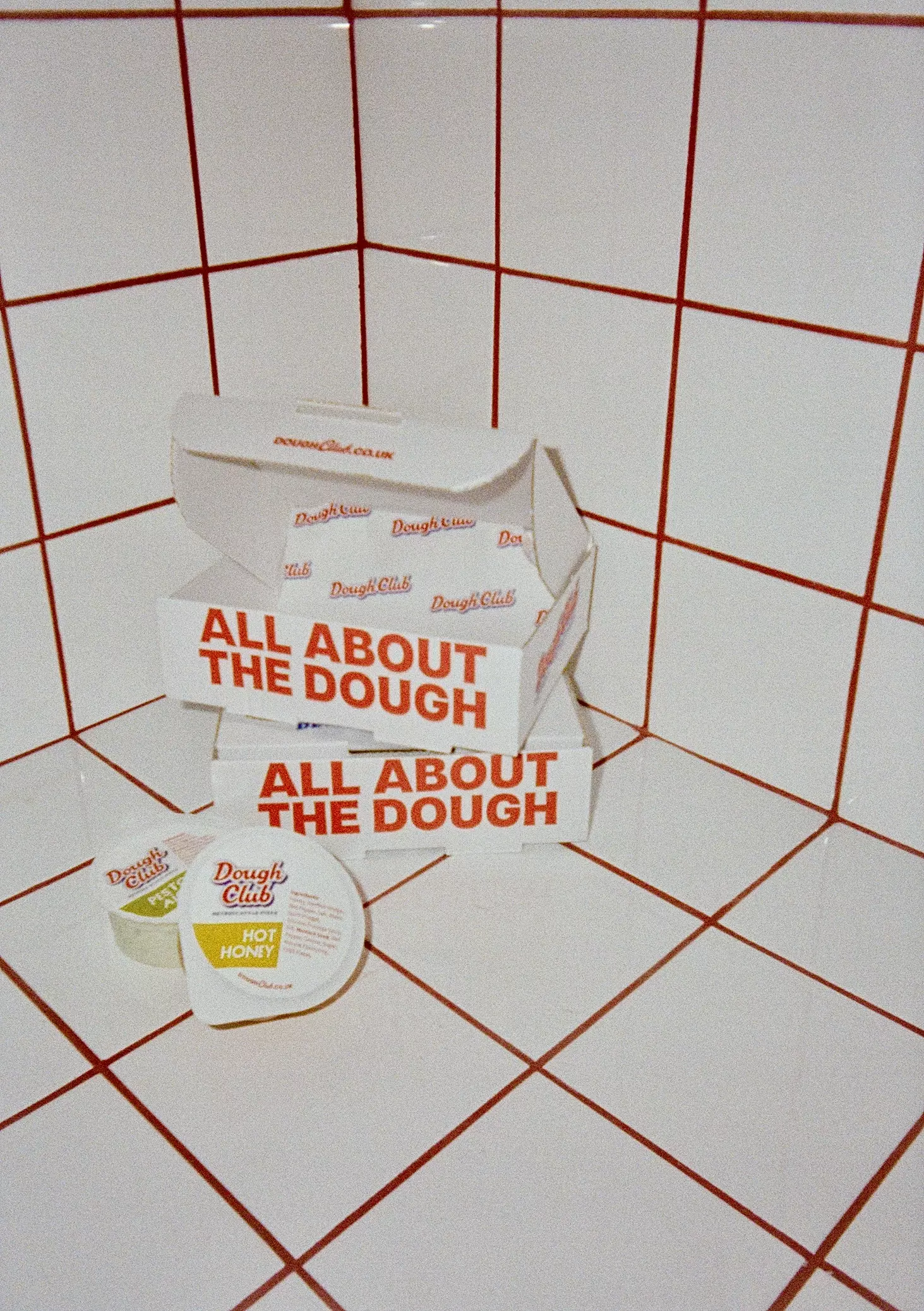 Dough Club Pizza packaging set against a white tiled wall