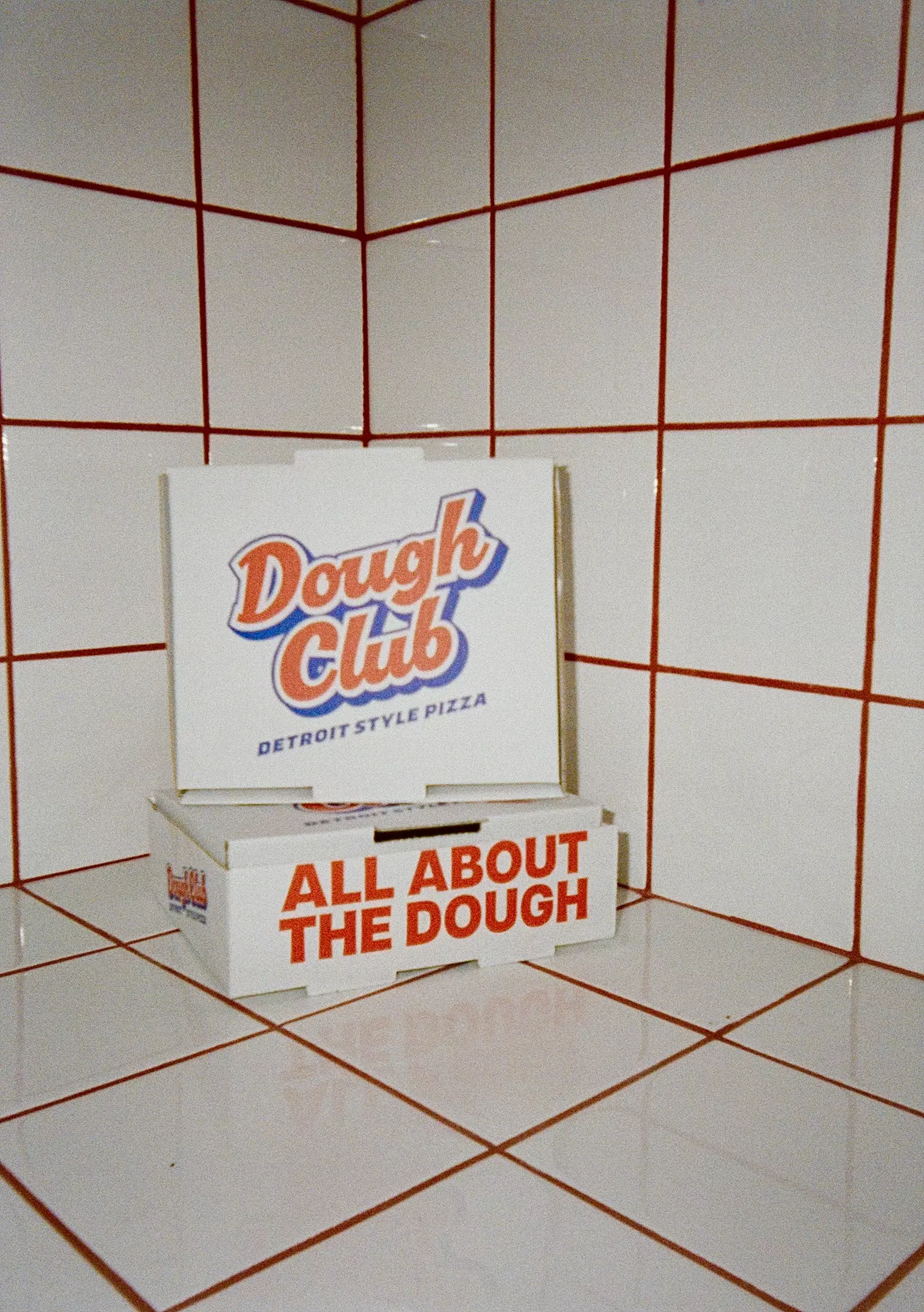 Dough Club Pizza packaging set against a white tiled wall